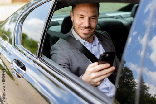 Businessman in a gray suit engaged with smartphone during sunny day car ride © BGStock72