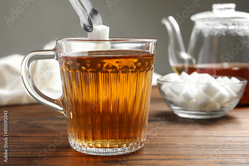 Adding sugar cube into cup of tea at wooden table, closeup