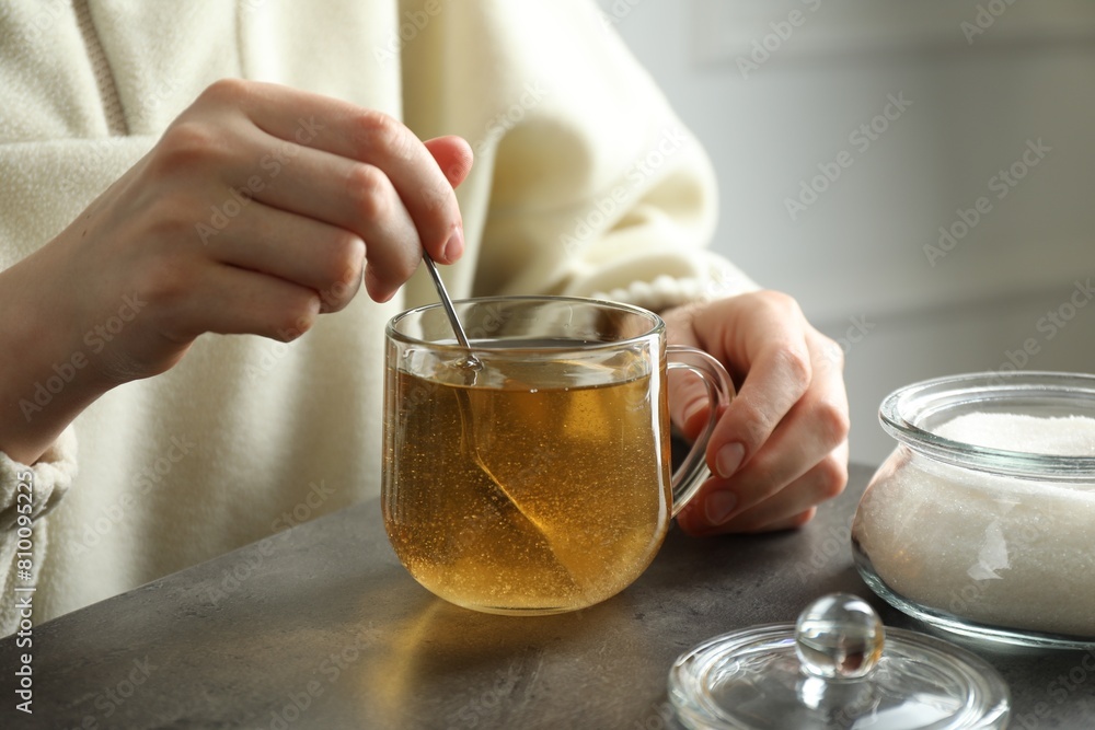Woman stirring sugar in tea at grey table, closeup Woman stirring sugar in tea at grey table, closeup