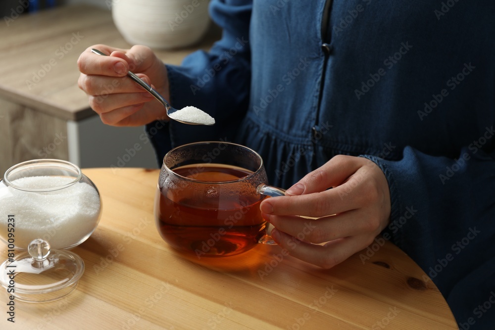 Woman adding sugar into aromatic tea at wooden table indoors, closeup Woman adding sugar into aromatic tea at wooden table indoors, closeup