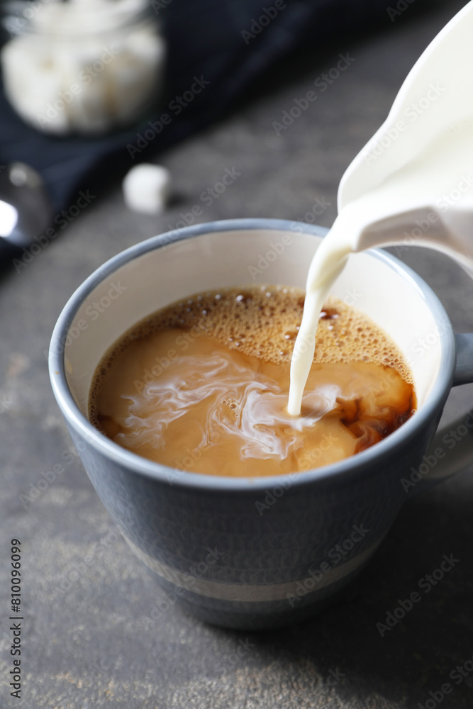 Pouring milk into cup of coffee on grey table, closeup Pouring milk into cup of coffee on grey table, closeup