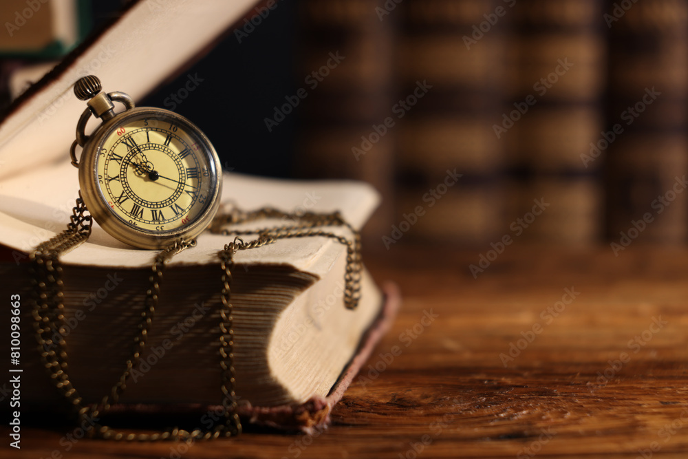 Pocket clock with chain and book on wooden table, closeup. Space for text