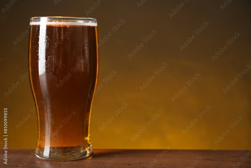 Glass with fresh beer on wooden table against dark background, closeup. Space for text