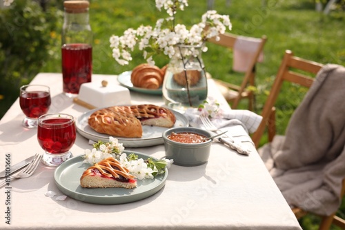 Stylish table setting with beautiful spring flowers  fruit drink and pie in garden