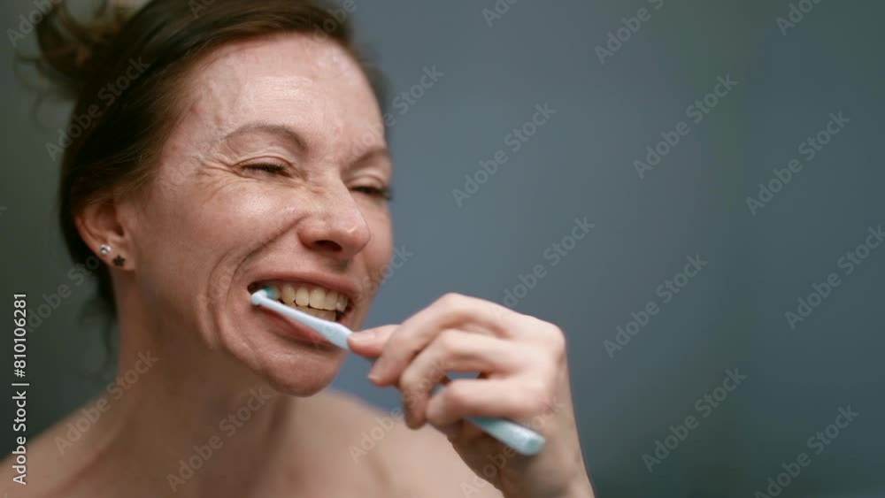 In her quiet corner of the bathroom, a middle-aged woman prefers brushing her teeth, enjoying the feeling of freshness and self-care. In her quiet corner of the bathroom, a middle-aged woman prefers brushing her teeth, enjoying the feeling of freshness and self-care.