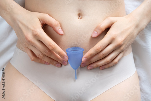 Woman using a blue menstrual cup, demonstrating its use in simple and intimate setting to highlight feminine health.