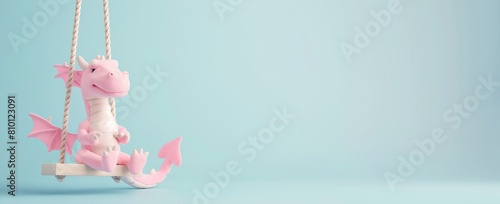 Cute baby pink dragon toy on the children's swing isolated against the light blue background, copy space.