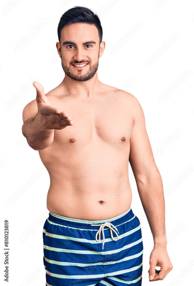 Young handsome man wearing swimwear smiling cheerful offering palm hand giving assistance and acceptance. Young handsome man wearing swimwear smiling cheerful offering palm hand giving assistance and acceptance.