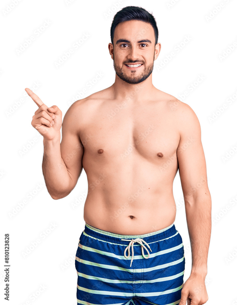 Young handsome man wearing swimwear with a big smile on face, pointing with hand finger to the side looking at the camera. Young handsome man wearing swimwear with a big smile on face, pointing with hand finger to the side looking at the camera.