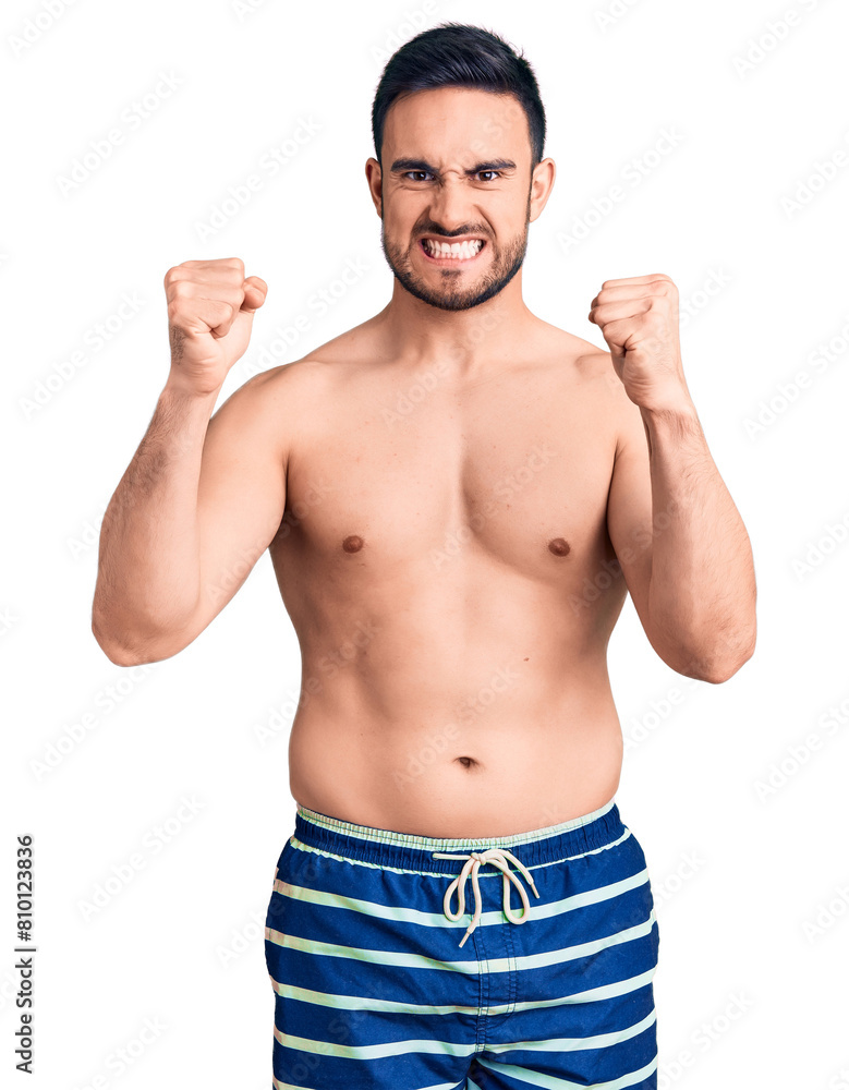 Young handsome man wearing swimwear angry and mad raising fists frustrated and furious while shouting with anger. rage and aggressive concept. Young handsome man wearing swimwear angry and mad raising fists frustrated and furious while shouting with anger. rage and aggressive concept.