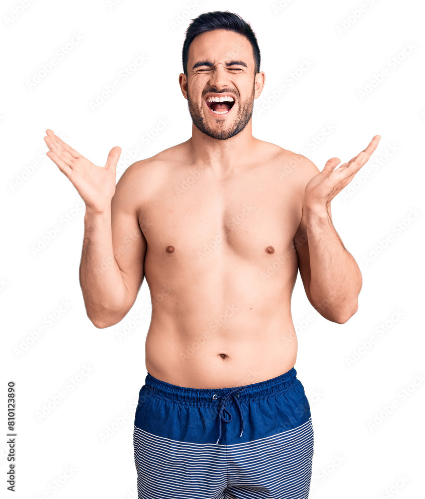Fototapeta premium Young handsome man wearing swimwear celebrating mad and crazy for success with arms raised and closed eyes screaming excited. winner concept