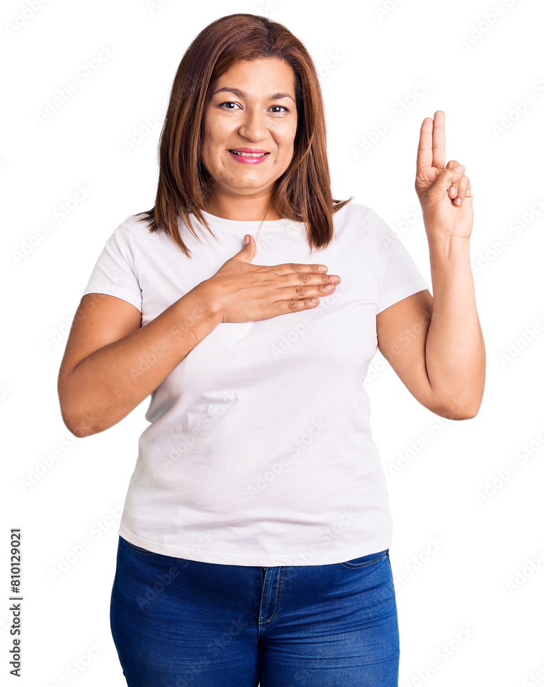 Middle age latin woman wearing casual white tshirt smiling swearing with hand on chest and fingers up, making a loyalty promise oath Middle age latin woman wearing casual white tshirt smiling swearing with hand on chest and fingers up, making a loyalty promise oath