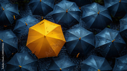 A collection of blue umbrellas with a single yellow umbrella standing out in the middle; a metaphor for uniqueness or nonconformity in a uniform group.