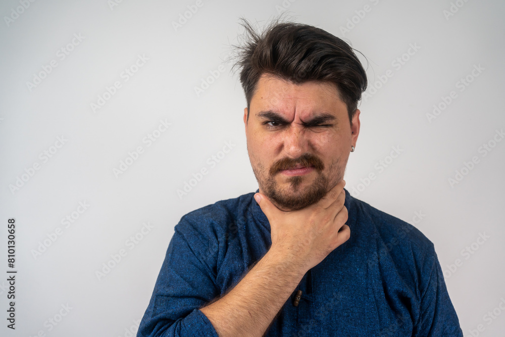 Young man having sore throat and touching his neck, wearing a blue shirt against light grey background. Hard to swallow. Touching painful neck, sore throat for flu, clod and infection