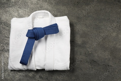 Blue karate belt and white kimono on gray textured background, top view. Space for text