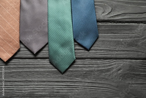 Different neckties on black wooden table, flat lay. Space for text