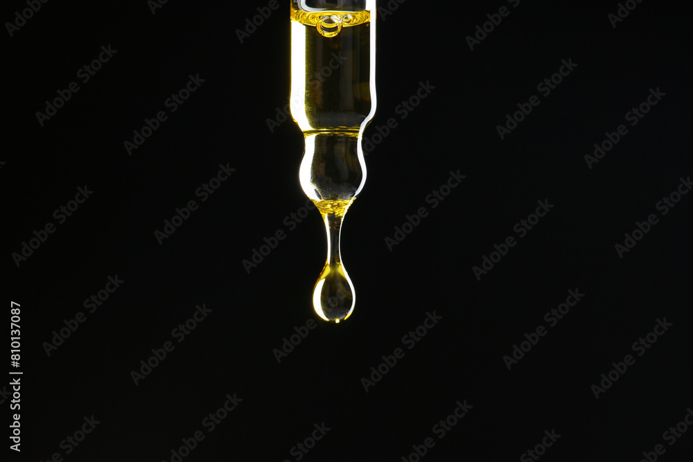 Dripping tincture from pipette on black background, closeup