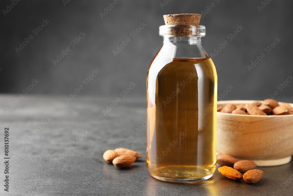 Almond oil in bottle, bowl and nuts on grey textured table, closeup. Space for text Almond oil in bottle, bowl and nuts on grey textured table, closeup. Space for text
