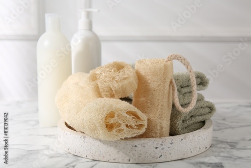 Loofah sponges, towels and cosmetic products on white marble table photo