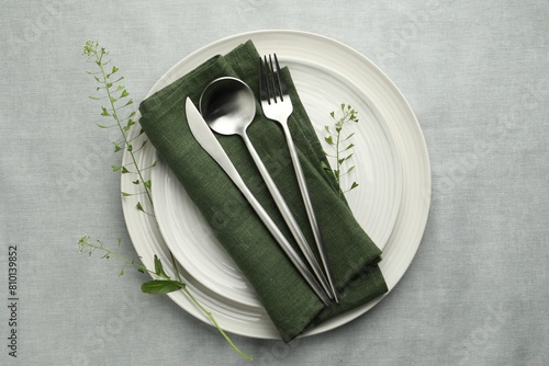 Stylish setting with cutlery, leaves and plates on grey table, top view