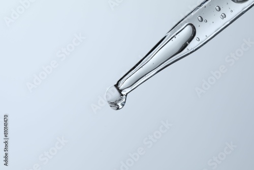 Dripping liquid from pipette on light blue background, closeup. Space for text