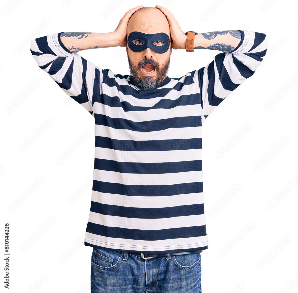 Young handsome man wearing burglar mask crazy and scared with hands on head, afraid and surprised of shock with open mouth Young handsome man wearing burglar mask crazy and scared with hands on head, afraid and surprised of shock with open mouth