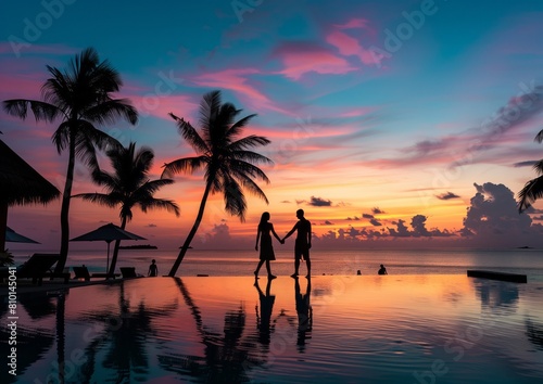 A couple holding hands and walking along the edge of an infinity pool at sunset, with palm trees silhouetted against the sky. The background is a beautiful beach scene in Maldives.  © samsusam