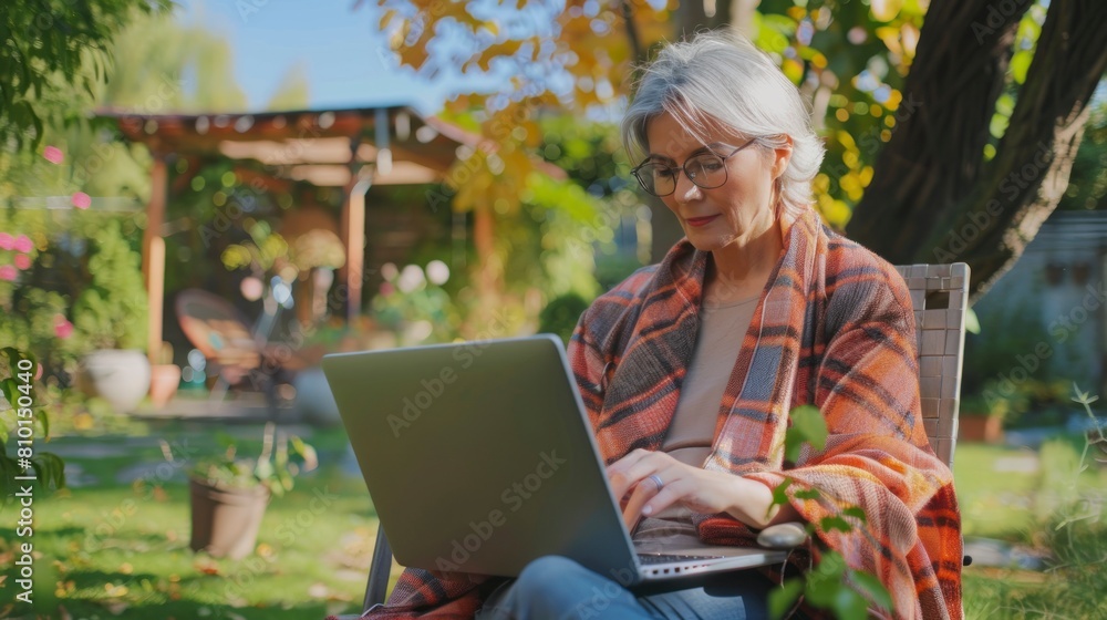 Obraz premium Modern handsome middle-aged woman in nice comfortable clothes working with laptop in home garden