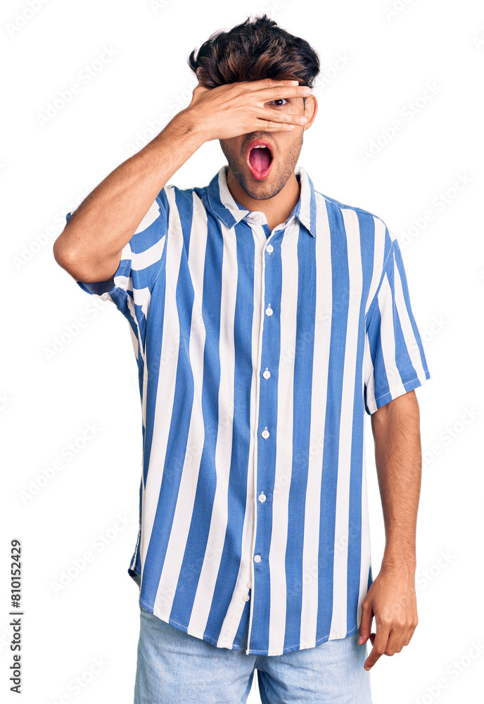Young hispanic man wearing casual clothes peeking in shock covering face and eyes with hand, looking through fingers with embarrassed expression. Young hispanic man wearing casual clothes peeking in shock covering face and eyes with hand, looking through fingers with embarrassed expression.