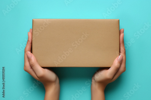 Mockup. Female hand holding brown rectangular cardboard box on light blue background. Generative AI © Anthony Paz