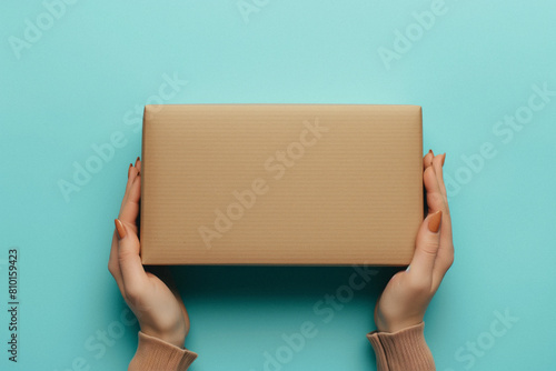 Mockup. Female hand holding brown rectangular cardboard box on light blue background. Generative AI