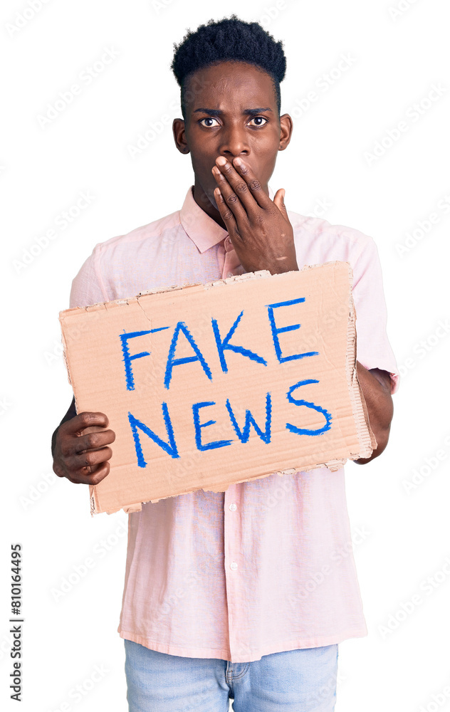 Φωτογραφία Young african american man holding fake news banner covering mouth with hand, shocked and afraid for mistake