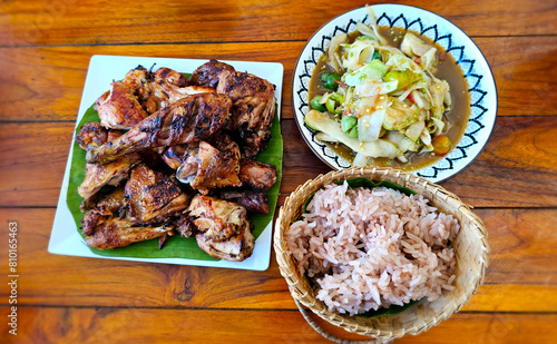 A traditional laos meal featuring succulent grilled chicken, spicy papaya salad, and a serving of sticky rice on a wooden table