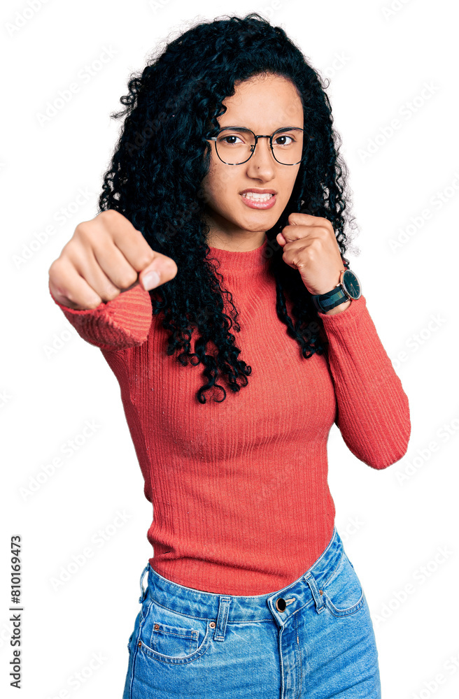 Young hispanic woman with curly hair wearing glasses punching fist to fight, aggressive and angry attack, threat and violence Young hispanic woman with curly hair wearing glasses punching fist to fight, aggressive and angry attack, threat and violence
