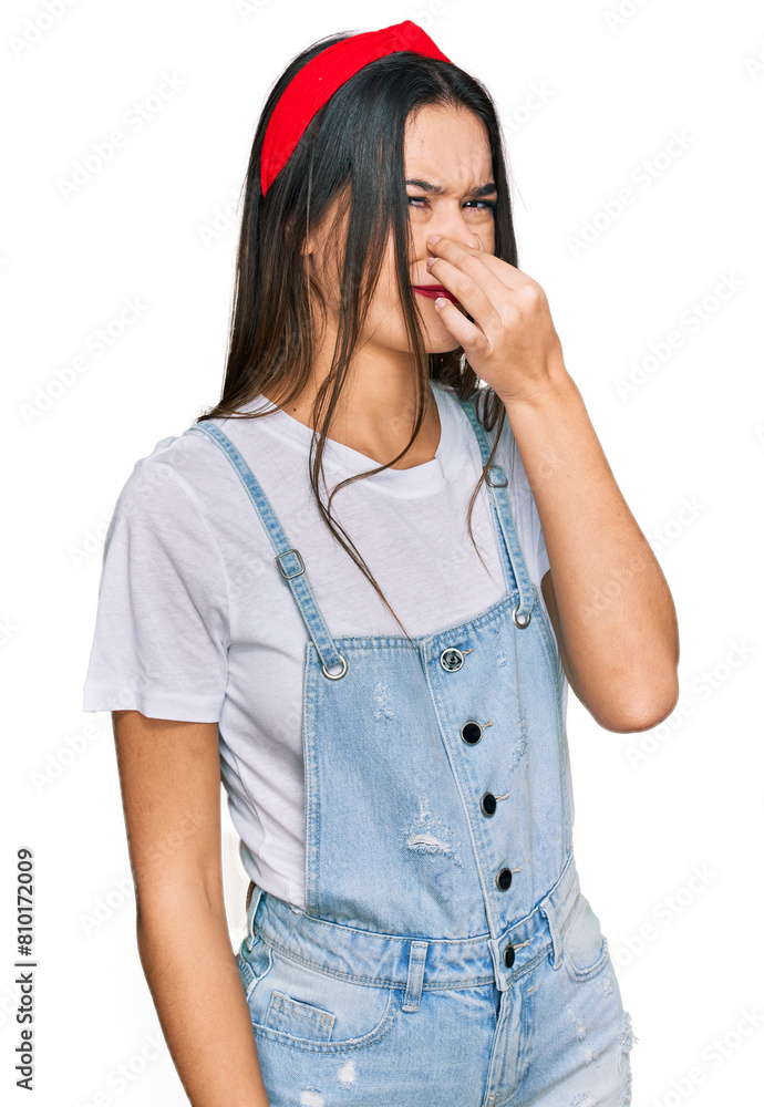 Young hispanic girl wearing casual clothes smelling something stinky and disgusting, intolerable smell, holding breath with fingers on nose. bad smell Young hispanic girl wearing casual clothes smelling something stinky and disgusting, intolerable smell, holding breath with fingers on nose. bad smell