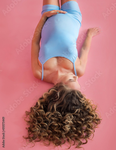 girl lying pregnant on pink background, top view, curly hair in foreground