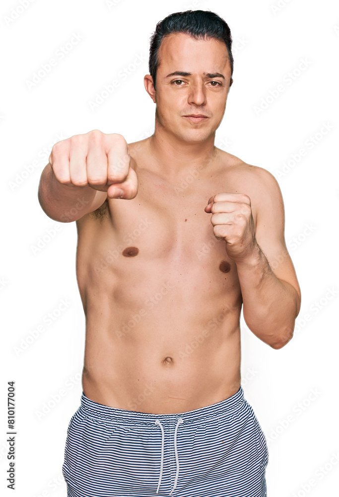 Handsome young man wearing swimwear shirtless punching fist to fight, aggressive and angry attack, threat and violence Handsome young man wearing swimwear shirtless punching fist to fight, aggressive and angry attack, threat and violence