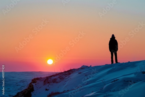 Lone silhouette standing proudly snow-capped outlined hues setting sun