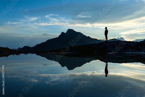 Lone figure mountain zenith outlined fading sunlight silent witness reflection peace