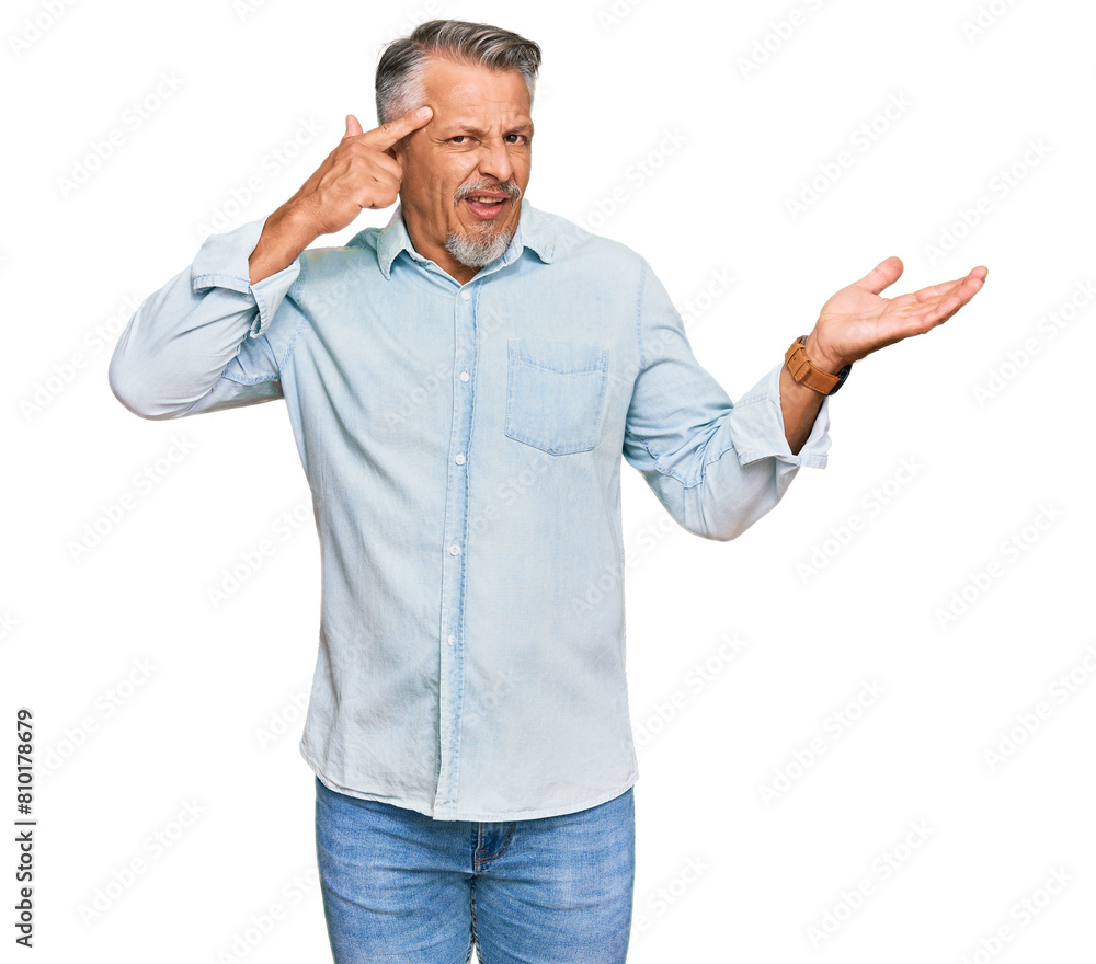 Middle age grey-haired man wearing casual clothes confused and annoyed with open palm showing copy space and pointing finger to forehead. think about it. Middle age grey-haired man wearing casual clothes confused and annoyed with open palm showing copy space and pointing finger to forehead. think about it.