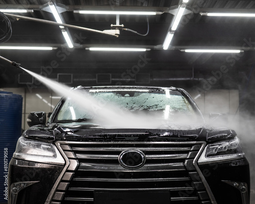A man washes foam off a black car with water at a car wash. © Михаил Решетников
