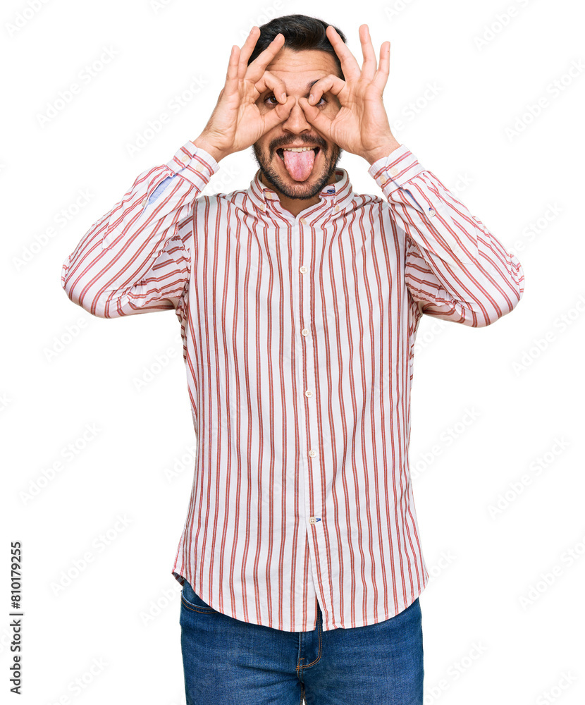 Young hispanic man wearing business shirt doing ok gesture like binoculars sticking tongue out, eyes looking through fingers. crazy expression. Young hispanic man wearing business shirt doing ok gesture like binoculars sticking tongue out, eyes looking through fingers. crazy expression.