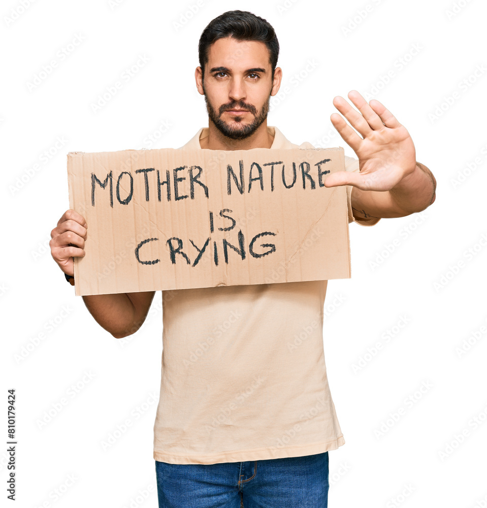 Young hispanic man holding mother nature is crying protest cardboard banner with open hand doing stop sign with serious and confident expression, defense gesture Young hispanic man holding mother nature is crying protest cardboard banner with open hand doing stop sign with serious and confident expression, defense gesture