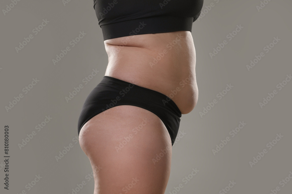 Fototapeta premium Woman with excessive belly fat on grey background, closeup. Overweight problem