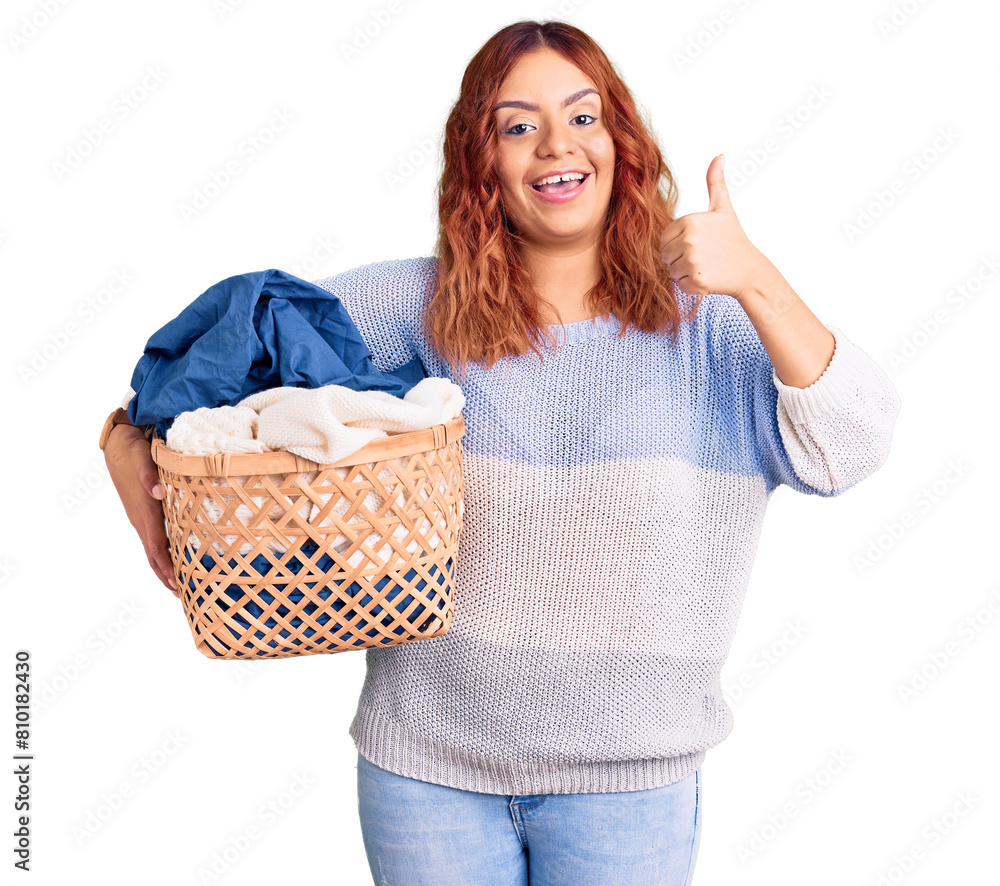 Young latin woman holding laundry basket smiling happy and positive, thumb up doing excellent and approval sign Young latin woman holding laundry basket smiling happy and positive, thumb up doing excellent and approval sign