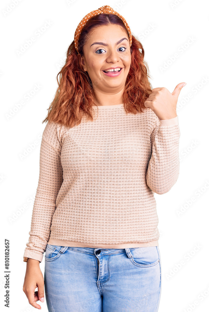 Obraz premium Young latin woman wearing casual clothes and diadem smiling with happy face looking and pointing to the side with thumb up.