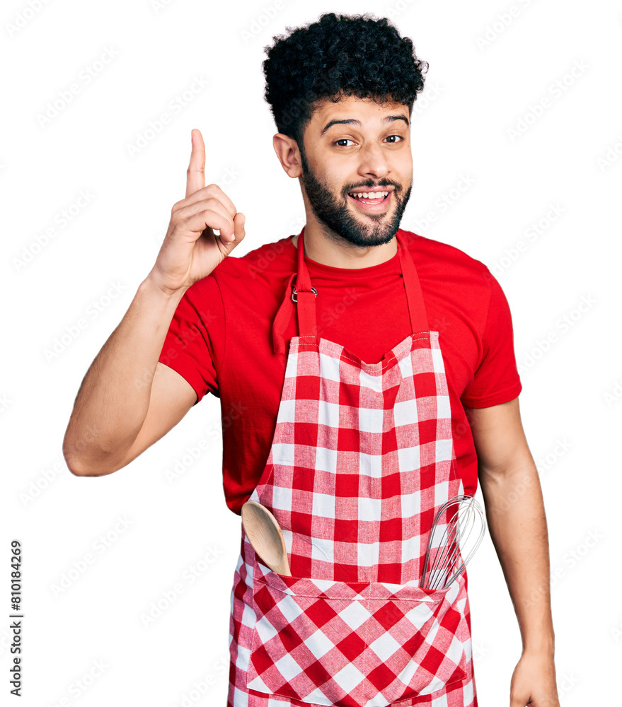 Young arab man with beard wearing cook apron pointing finger up with successful idea. exited and happy. number one. Young arab man with beard wearing cook apron pointing finger up with successful idea. exited and happy. number one.