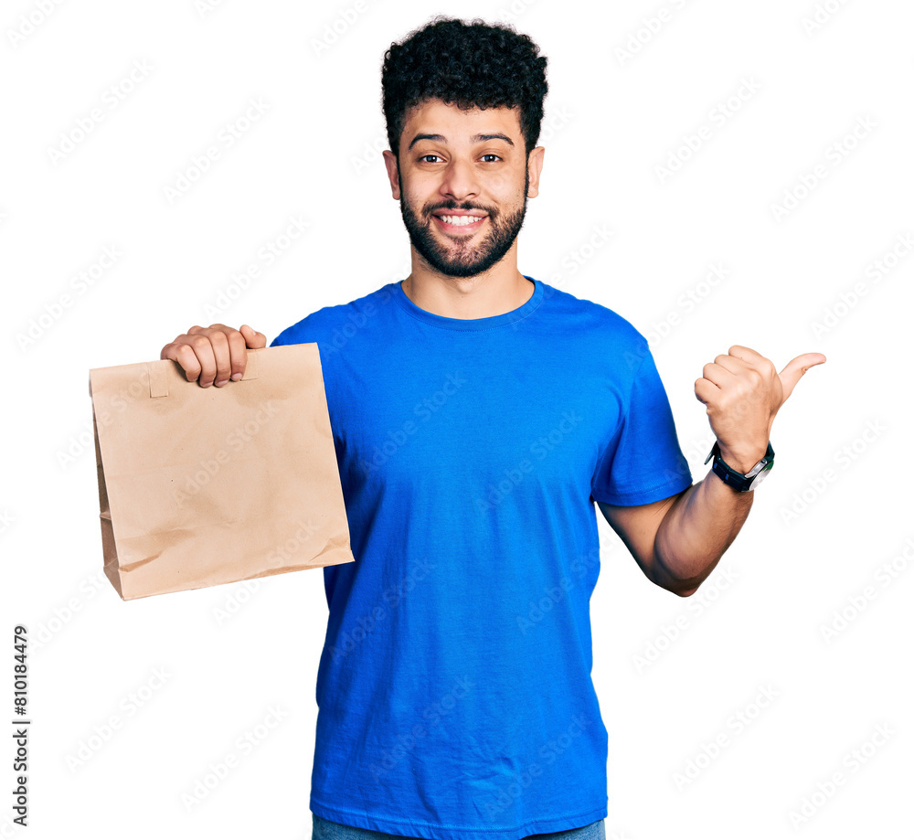 Young arab man with beard holding take away paper bag pointing thumb up to the side smiling happy with open mouth Young arab man with beard holding take away paper bag pointing thumb up to the side smiling happy with open mouth
