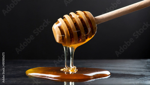 Sweet viscous honey made by bees dripping from wooden dipper with spaced grooves on black background