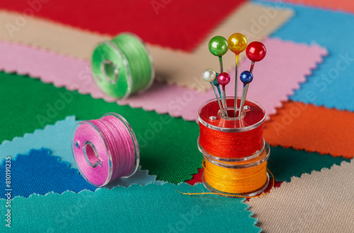 sewing kit made of spools of colored threads. Background of colored scraps of fabric.